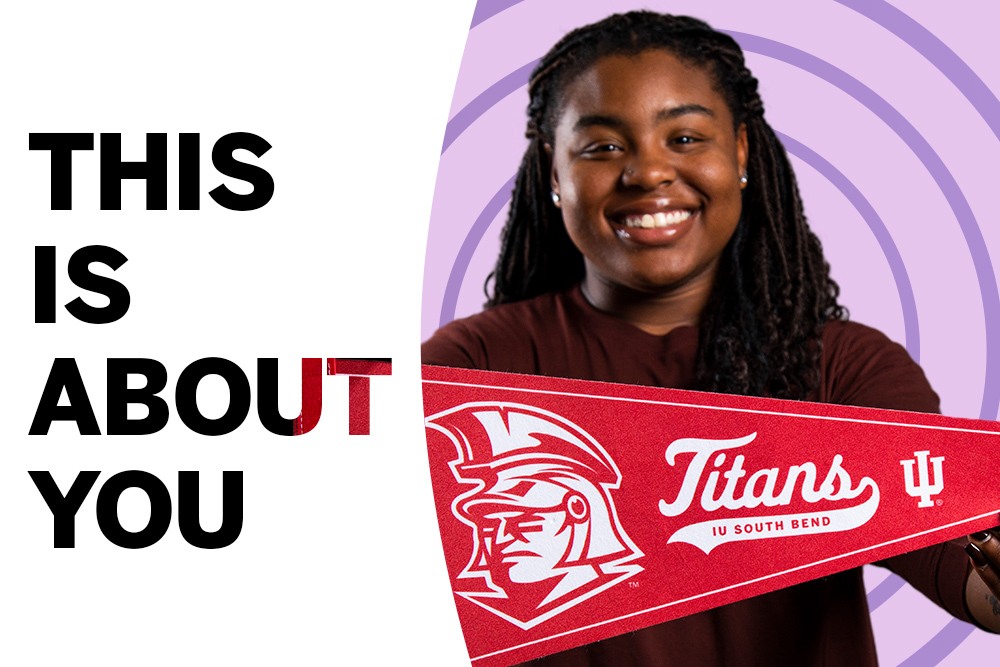 A student in front of a purple background holding a Titans spirit banner with the text THIS IS ABOUT YOU on her left